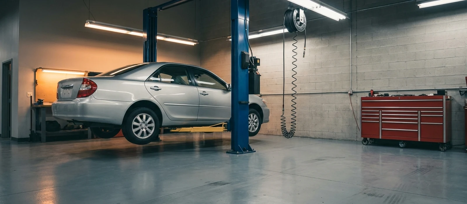 A silver sedan raised on a blue two-post hoist in a clean auto repair shop, with a tool chest against the far wall